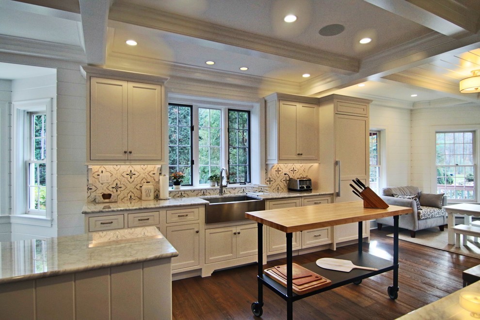 Open concept kitchen - large transitional l-shaped laminate floor and brown floor open concept kitchen idea in Boston with a farmhouse sink, recessed-panel cabinets, white cabinets, marble countertops, white backsplash, marble backsplash, paneled appliances and an island