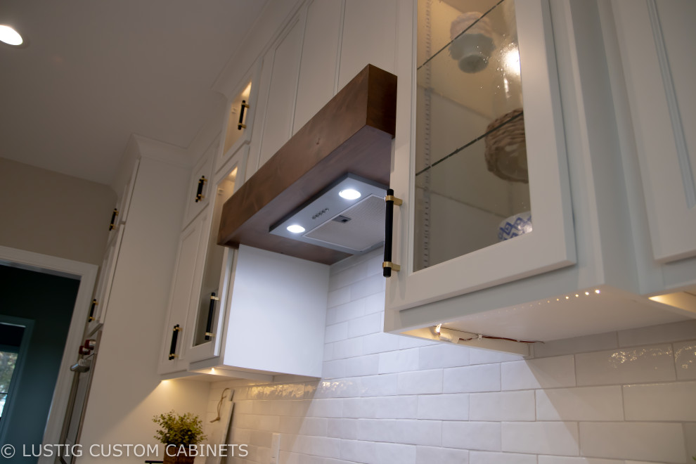 Example of a large transitional l-shaped laminate floor and brown floor open concept kitchen design with an undermount sink, flat-panel cabinets, white cabinets, quartz countertops, white backsplash, ceramic backsplash, stainless steel appliances, an island and white countertops