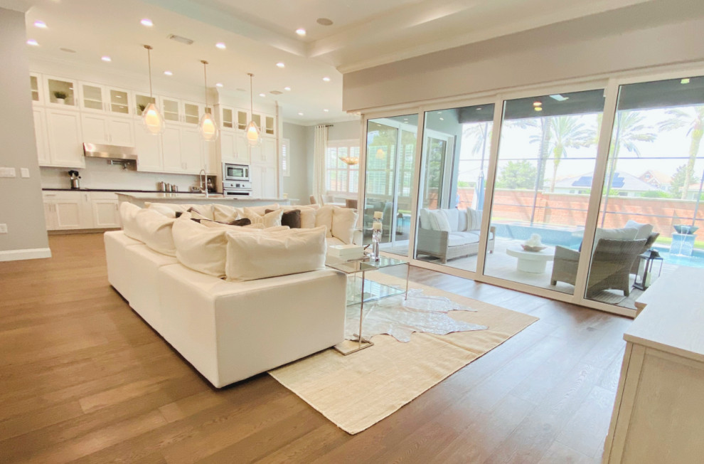 Photo of an expansive transitional open concept family room in Tampa with grey walls, light hardwood floors, a wall-mounted tv, brown floor and recessed.
