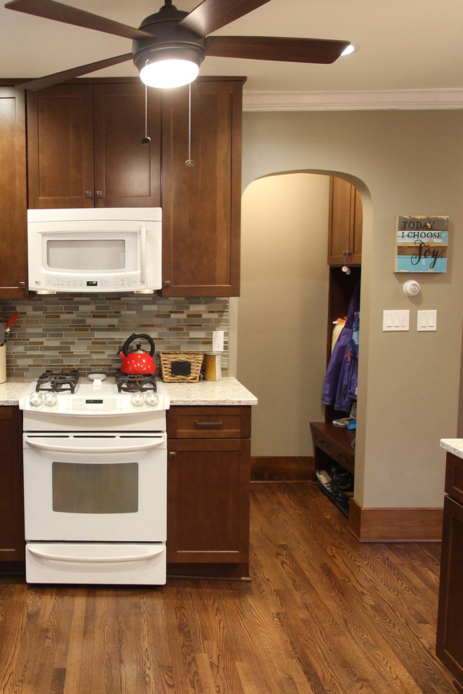Photo of a mid-sized transitional l-shaped kitchen pantry in Cleveland with an undermount sink, shaker cabinets, medium wood cabinets, quartz benchtops, brown splashback, glass tile splashback, white appliances, medium hardwood floors, with island and brown floor.
