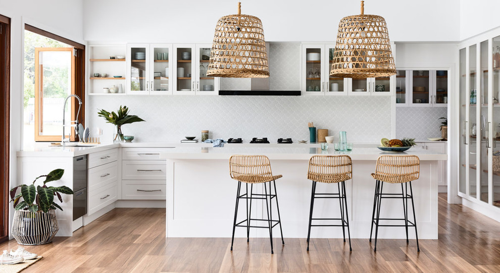 This is an example of a beach style u-shaped kitchen in Sydney with an undermount sink, shaker cabinets, white cabinets, white splashback, dark hardwood floors, with island, brown floor and white benchtop.