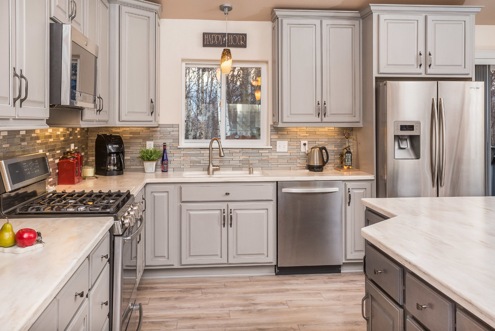 Example of a mid-sized transitional l-shaped open concept kitchen design with an undermount sink, raised-panel cabinets, gray cabinets, solid surface countertops, metallic backsplash, mosaic tile backsplash, stainless steel appliances and an island