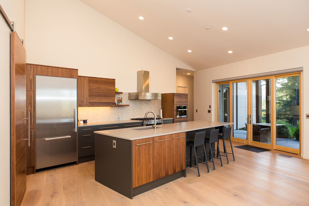 Large contemporary open plan kitchen in Portland with an undermount sink, quartz benchtops, multi-coloured splashback, stainless steel appliances, light hardwood floors and with island.