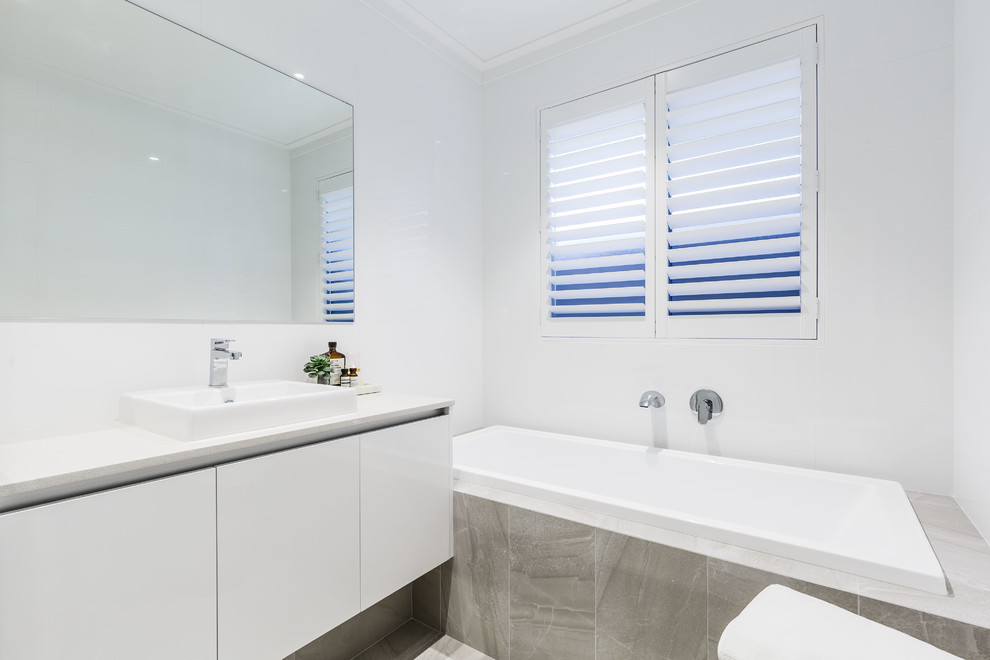 Contemporary kids bathroom in Perth with flat-panel cabinets, white cabinets, a drop-in tub, a corner shower, white tile, porcelain tile, white walls, porcelain floors, a drop-in sink, solid surface benchtops, grey floor, a hinged shower door and white benchtops.