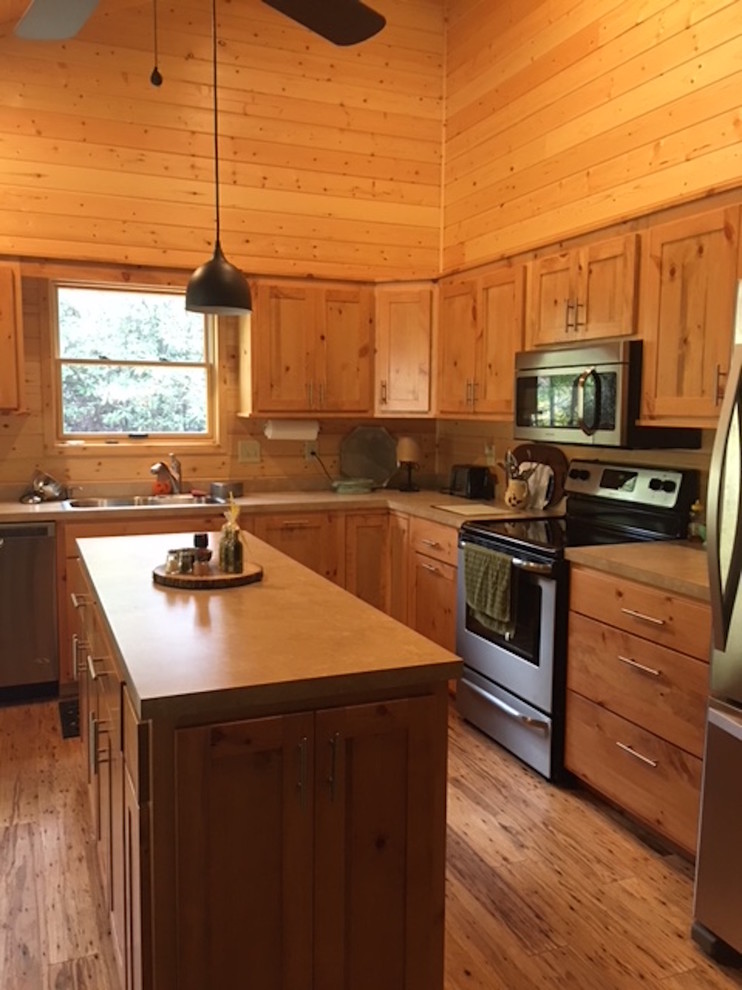 Example of a large mountain style l-shaped medium tone wood floor and brown floor kitchen design with a double-bowl sink, shaker cabinets, light wood cabinets, solid surface countertops, brown backsplash, wood backsplash and stainless steel appliances