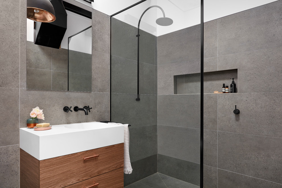 Photo of a small industrial 3/4 bathroom in Melbourne with flat-panel cabinets, dark wood cabinets, gray tile, porcelain tile, porcelain floors, an integrated sink, solid surface benchtops, grey floor, an open shower, a corner shower and grey walls.