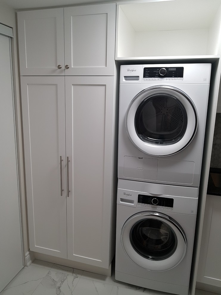 Design ideas for a large transitional single-wall dedicated laundry room in Toronto with an undermount sink, shaker cabinets, white cabinets, quartz benchtops, marble floors, a stacked washer and dryer and white floor.