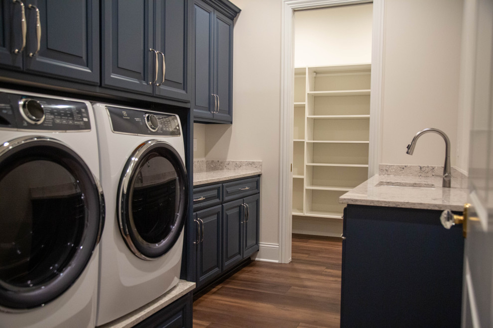 Expansive transitional galley dedicated laundry room in Indianapolis with an undermount sink, raised-panel cabinets, blue cabinets, granite benchtops, beige walls, laminate floors, a side-by-side washer and dryer, brown floor and multi-coloured benchtop.