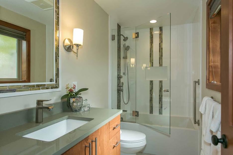 Mid-sized tropical master bathroom in Portland with flat-panel cabinets, medium wood cabinets, an alcove tub, a shower/bathtub combo, a one-piece toilet, green tile, stone tile, beige walls, porcelain floors and an undermount sink.