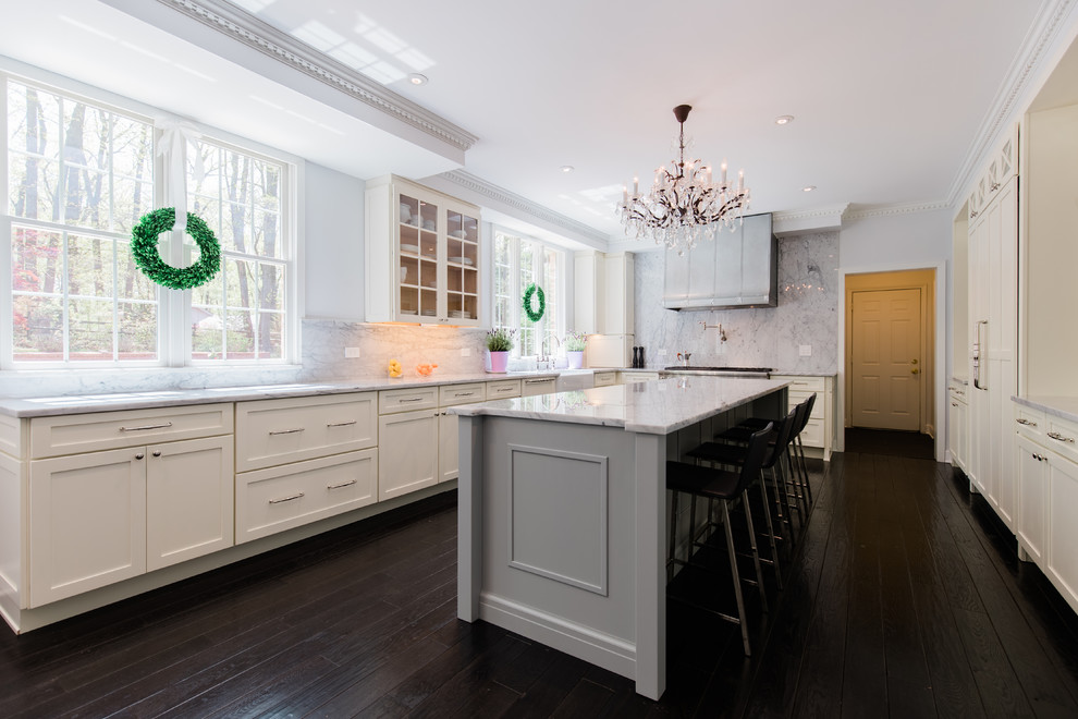 Photo of a large modern single-wall eat-in kitchen in DC Metro with a farmhouse sink, flat-panel cabinets, white cabinets, marble benchtops, white splashback, marble splashback, panelled appliances, dark hardwood floors, with island, brown floor and white benchtop.