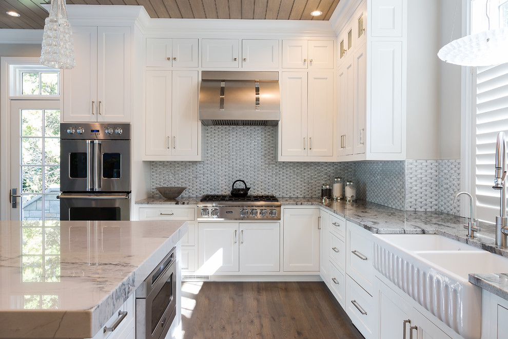 Eat-in kitchen - large transitional l-shaped medium tone wood floor eat-in kitchen idea with a farmhouse sink, recessed-panel cabinets, white cabinets, marble countertops, gray backsplash, porcelain backsplash, stainless steel appliances and an island