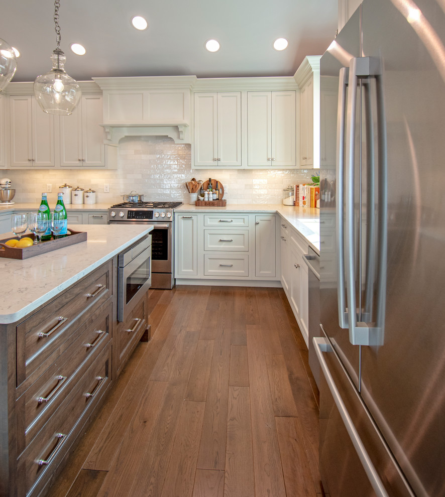 Inspiration for a transitional medium tone wood floor, brown floor and vaulted ceiling eat-in kitchen remodel with an undermount sink, shaker cabinets, white cabinets, quartz countertops, white backsplash, ceramic backsplash, stainless steel appliances, an island and white countertops