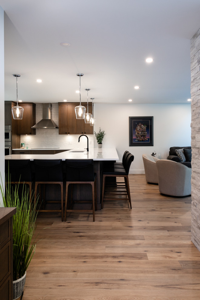 Open concept kitchen - mid-sized transitional u-shaped medium tone wood floor and brown floor open concept kitchen idea in Vancouver with an undermount sink, shaker cabinets, dark wood cabinets, quartz countertops, white backsplash, porcelain backsplash, stainless steel appliances, a peninsula and white countertops