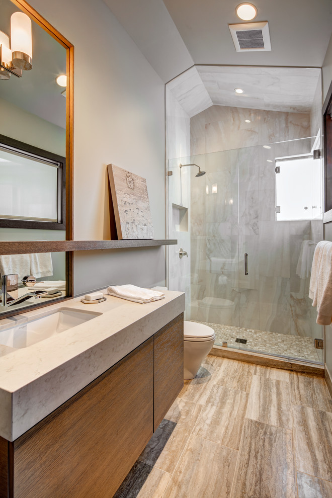 Photo of a mid-sized modern master bathroom in Salt Lake City with flat-panel cabinets, dark wood cabinets, an alcove shower, a one-piece toilet, beige tile, gray tile, stone slab, grey walls, porcelain floors, an undermount sink, laminate benchtops, brown floor and a hinged shower door.