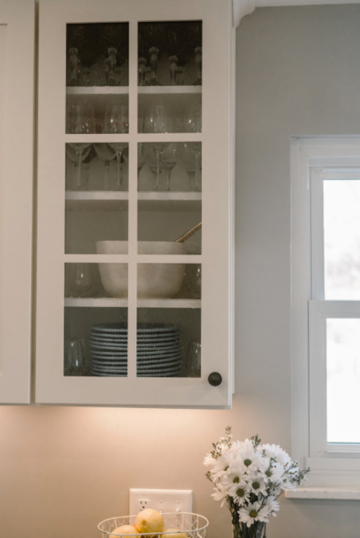 Mid-sized transitional l-shaped medium tone wood floor and brown floor eat-in kitchen photo in Columbus with a farmhouse sink, shaker cabinets, white cabinets, solid surface countertops, gray backsplash, matchstick tile backsplash, stainless steel appliances and no island