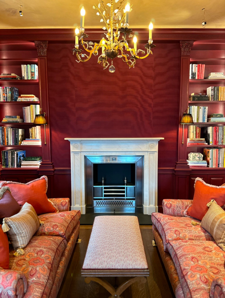 Photo of a large victorian enclosed living room with a reading nook, a standard fireplace, a wooden fireplace surround, brown floors, wallpapered walls and feature lighting.