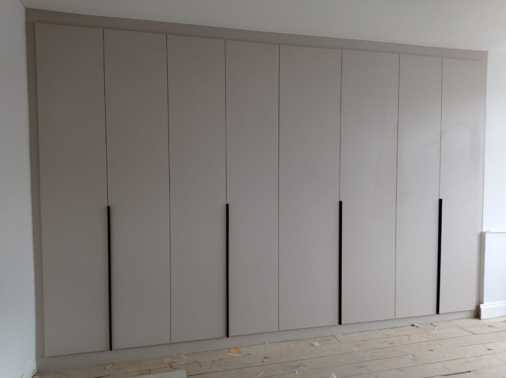 Mid-sized traditional gender-neutral storage and wardrobe in London with flat-panel cabinets, white cabinets, laminate floors, brown floor and recessed.