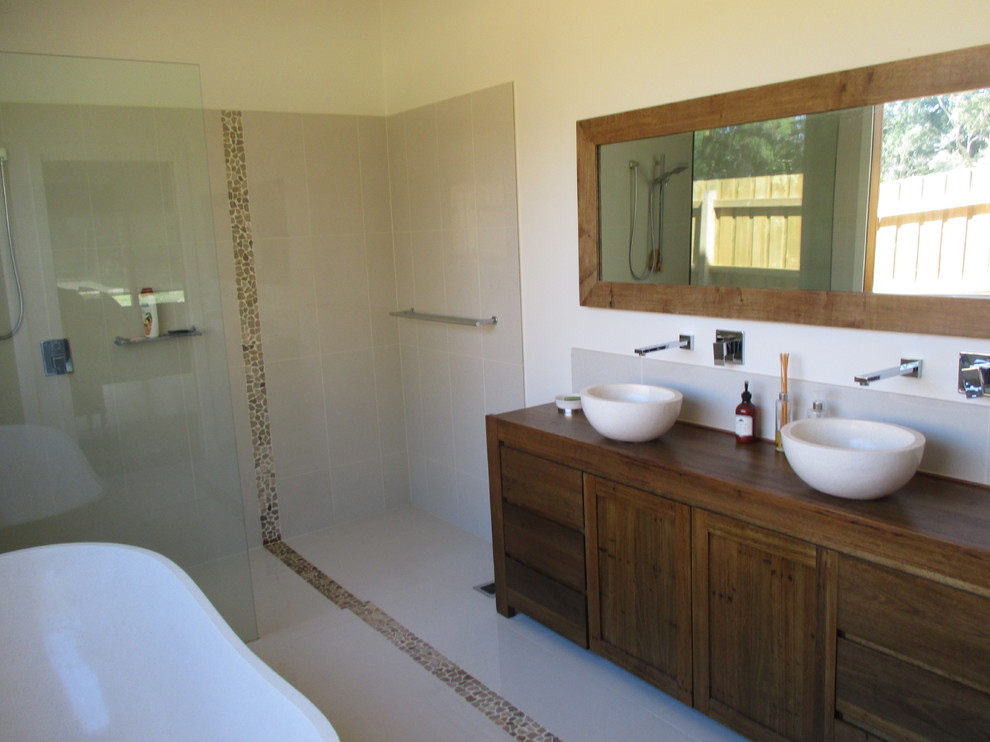 Design ideas for a mid-sized country master bathroom in Melbourne with furniture-like cabinets, dark wood cabinets, a freestanding tub, an open shower, gray tile, porcelain tile, white walls, porcelain floors, wood benchtops and an open shower.