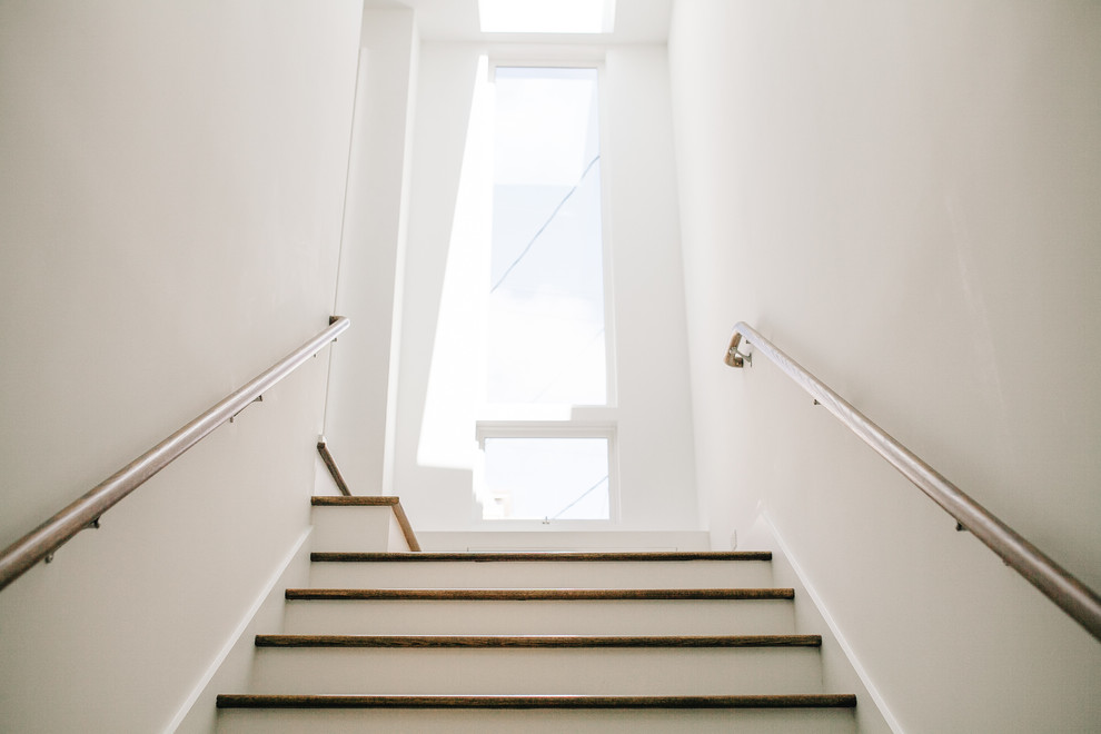 Mid-sized minimalist galley medium tone wood floor staircase photo in San Francisco with an undermount sink, recessed-panel cabinets, white cabinets, solid surface countertops, white backsplash, stone slab backsplash and paneled appliances