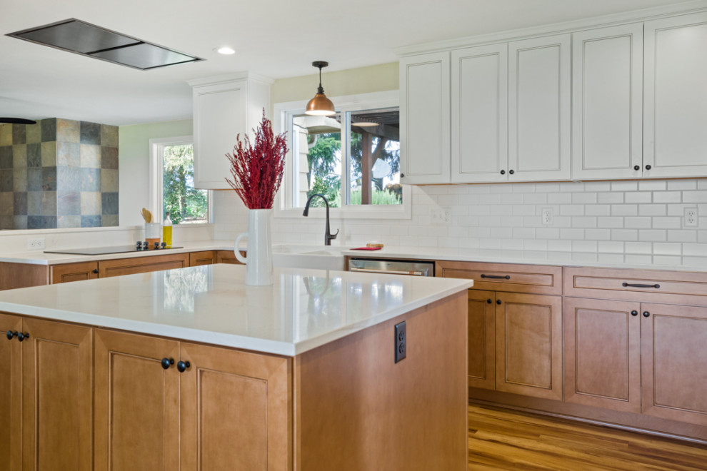 Example of a mid-sized transitional l-shaped medium tone wood floor and brown floor eat-in kitchen design with a farmhouse sink, shaker cabinets, white cabinets, quartz countertops, white backsplash, subway tile backsplash, stainless steel appliances, an island and white countertops