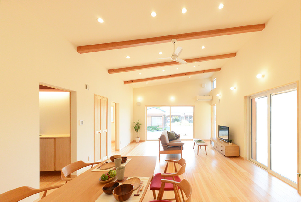 Cette image montre une grande salle à manger ouverte sur le salon asiatique avec un mur blanc, un sol en bois brun, aucune cheminée, un sol beige, poutres apparentes et éclairage.