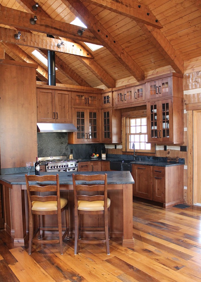 Photo of a large country u-shaped eat-in kitchen in Other with a farmhouse sink, glass-front cabinets, dark wood cabinets, granite benchtops, black splashback, stone slab splashback, stainless steel appliances, medium hardwood floors and a peninsula.