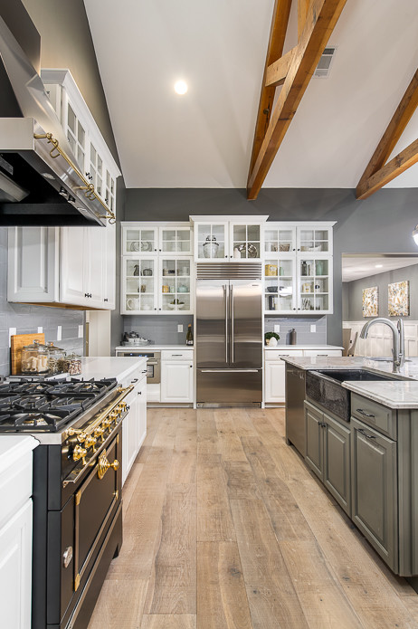 Inspiration for a large transitional light wood floor open concept kitchen remodel in Phoenix with a farmhouse sink, raised-panel cabinets, white cabinets, marble countertops, gray backsplash, glass tile backsplash, stainless steel appliances and an island
