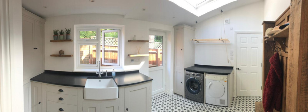 Inspiration for a mid-sized traditional l-shaped utility room in Berkshire with a farmhouse sink, shaker cabinets, grey cabinets, quartzite benchtops, white walls, porcelain floors, an integrated washer and dryer, black floor and black benchtop.