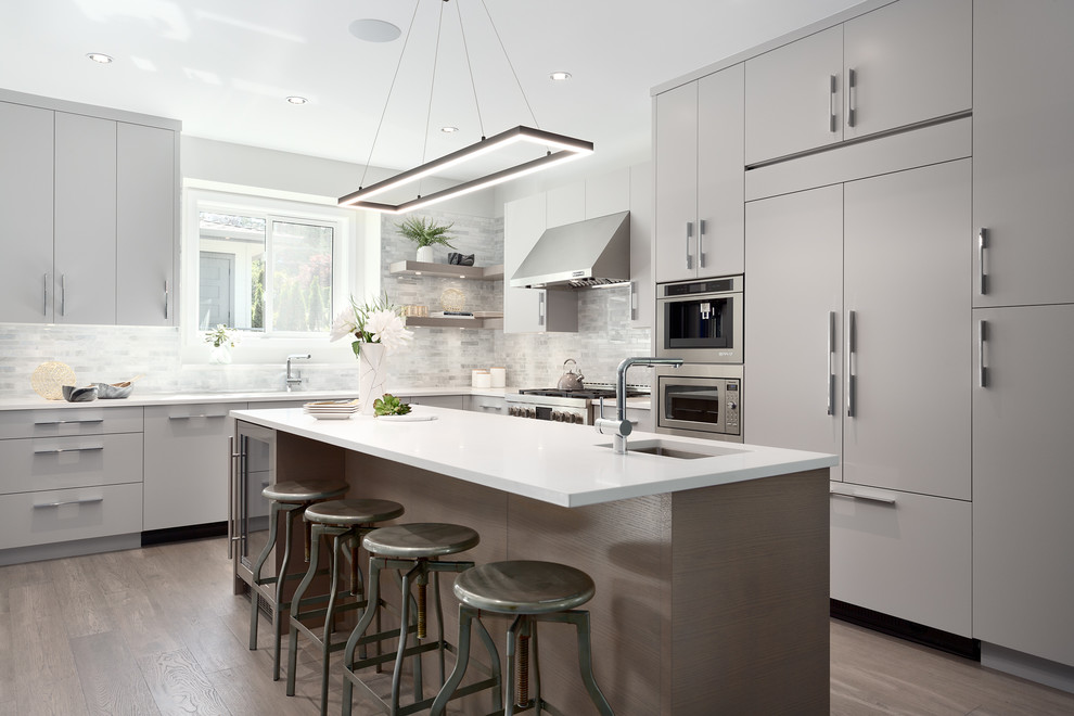 Mid-sized contemporary l-shaped open plan kitchen in Vancouver with flat-panel cabinets, grey cabinets, white splashback, stone tile splashback, panelled appliances, with island, brown floor, white benchtop, a double-bowl sink, medium hardwood floors and solid surface benchtops.