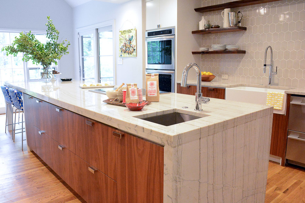 This is an example of a contemporary galley eat-in kitchen in Atlanta with a farmhouse sink, medium wood cabinets, quartzite benchtops, grey splashback, ceramic splashback, stainless steel appliances, medium hardwood floors and with island.