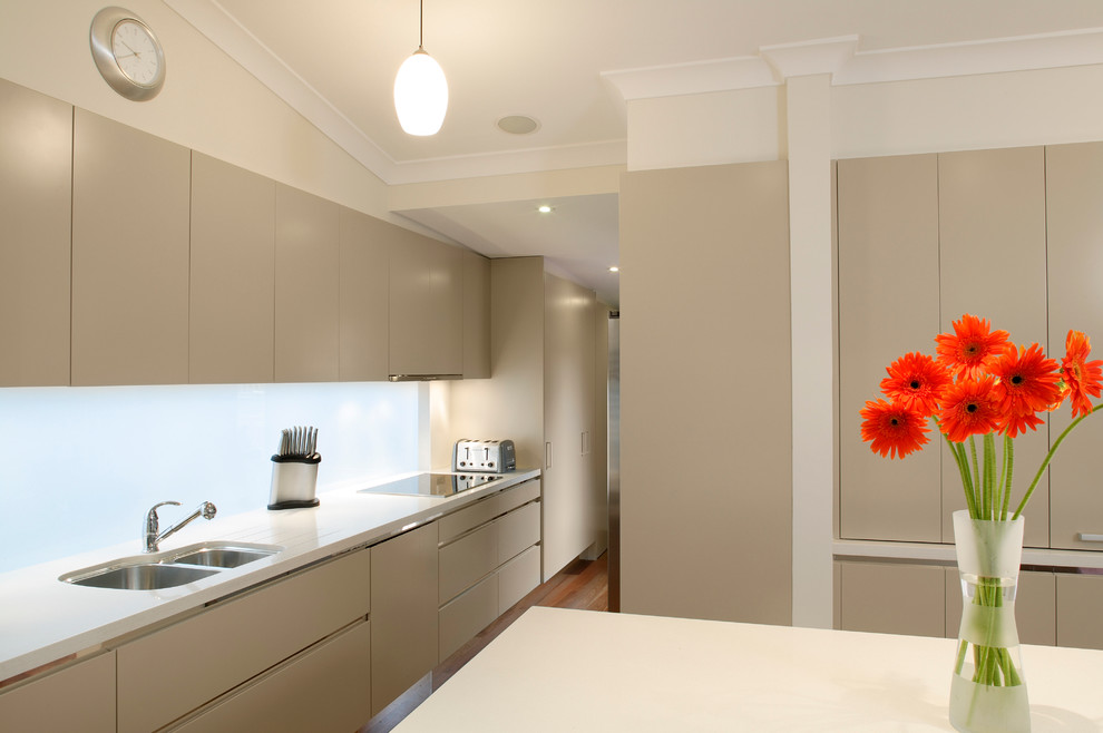 This is an example of a mid-sized contemporary galley eat-in kitchen in Sydney with an undermount sink, flat-panel cabinets, beige cabinets, granite benchtops, white splashback, stainless steel appliances, medium hardwood floors, with island and glass sheet splashback.