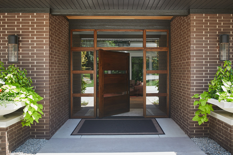 This is an example of a midcentury entryway in Grand Rapids with a pivot front door and a dark wood front door.