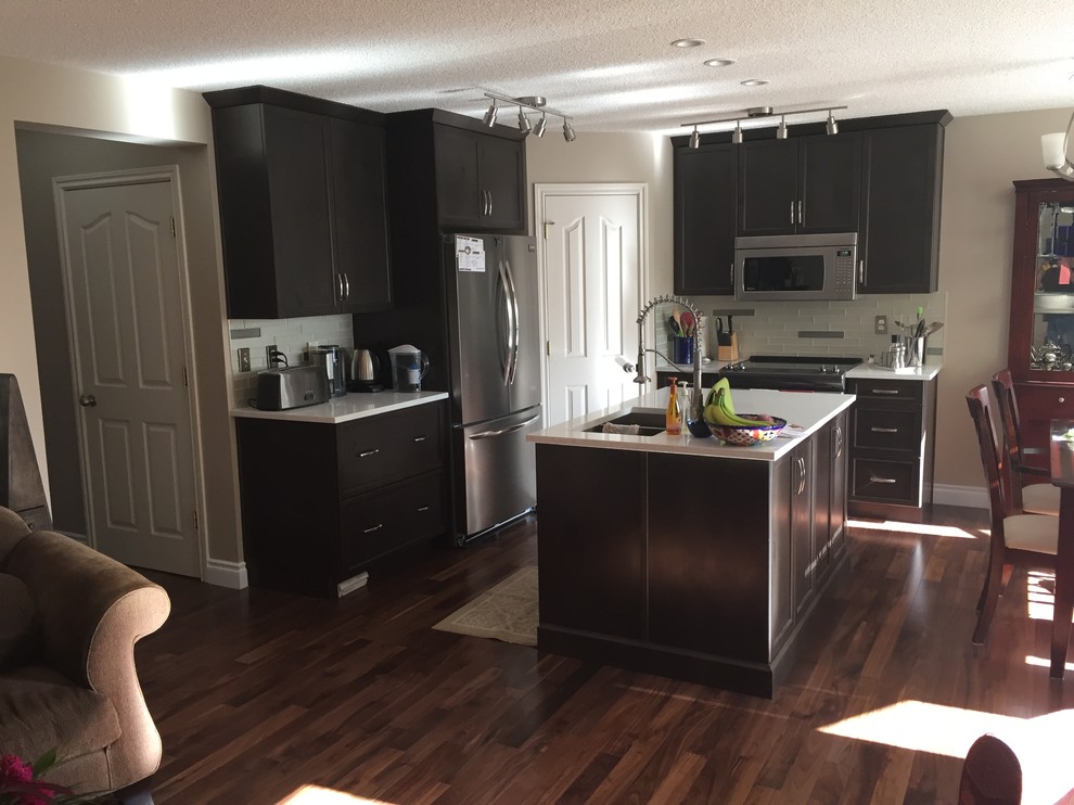 Inspiration for a mid-sized transitional single-wall dark wood floor and brown floor open concept kitchen remodel in Calgary with a double-bowl sink, shaker cabinets, dark wood cabinets, white backsplash, subway tile backsplash, stainless steel appliances and an island
