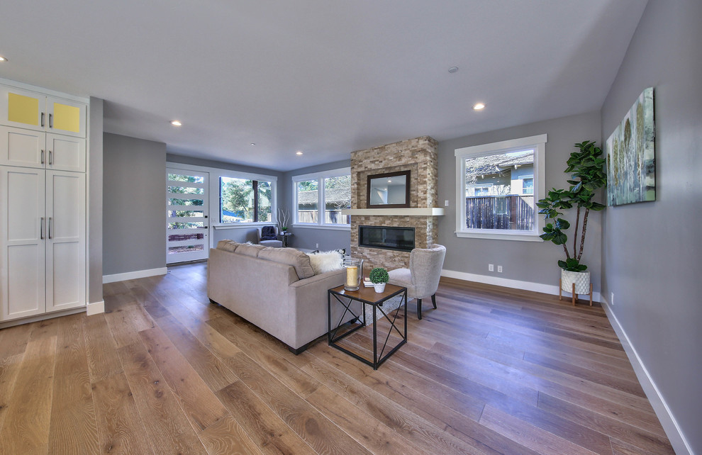 This is an example of a mid-sized transitional formal open concept living room in Other with grey walls, light hardwood floors, a standard fireplace, a stone fireplace surround, no tv and brown floor.