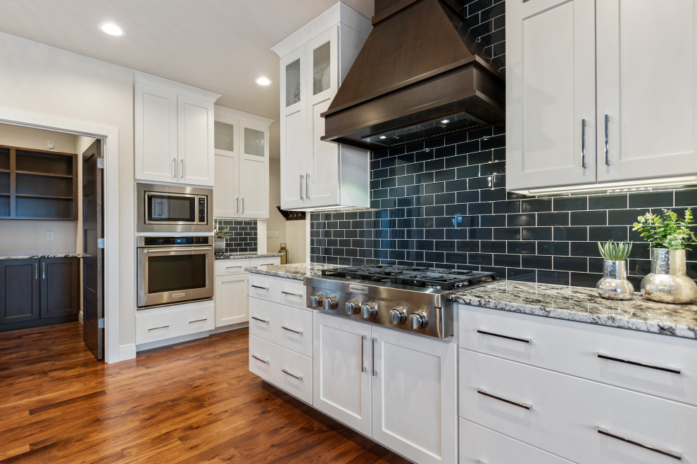 Inspiration for a mid-sized transitional l-shaped medium tone wood floor and brown floor eat-in kitchen remodel with an undermount sink, shaker cabinets, white cabinets, granite countertops, blue backsplash, subway tile backsplash, stainless steel appliances, an island and multicolored countertops
