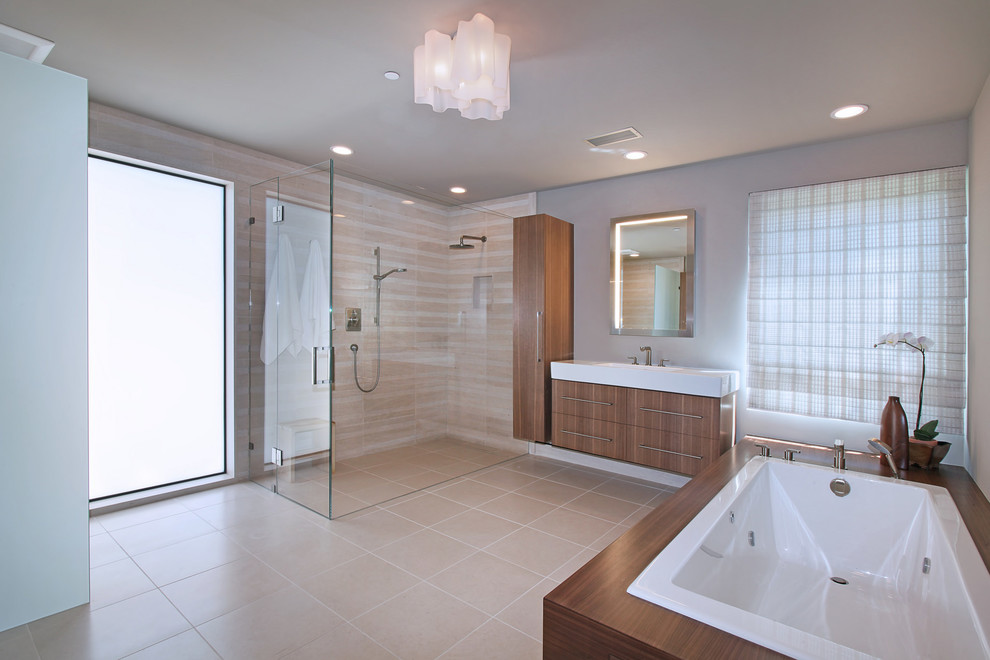 Inspiration for a midcentury master bathroom in Orange County with flat-panel cabinets, medium wood cabinets, a drop-in tub, a curbless shower, stone tile, limestone floors, beige tile and grey walls.