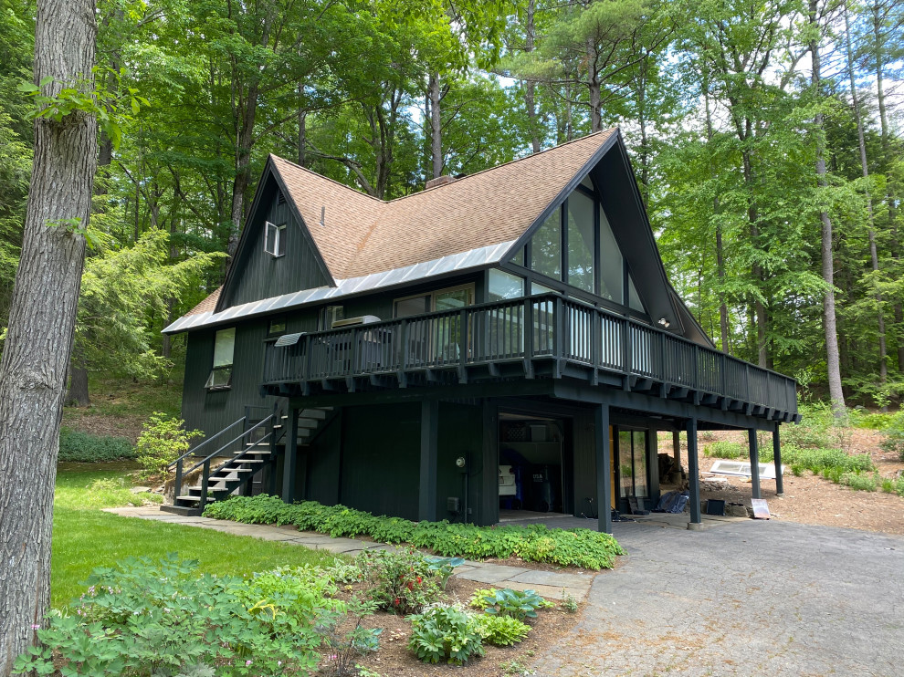 Aménagement d'une façade de maison noire rétro en bois et planches et couvre-joints de taille moyenne et à un étage avec un toit en shingle et un toit marron.