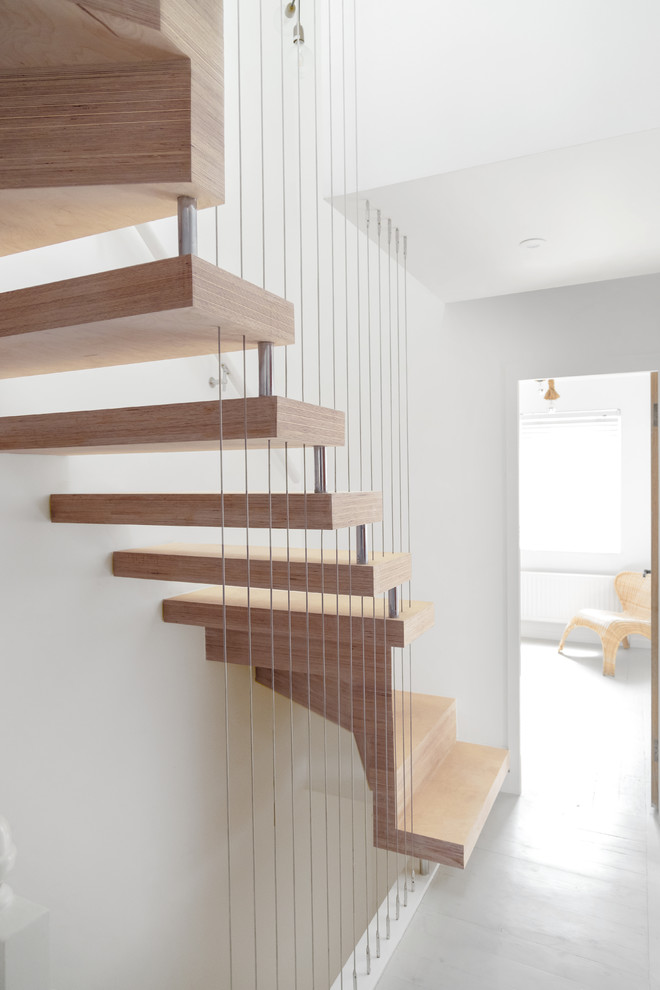 Inspiration for a mid-sized contemporary wood u-shaped staircase in London with open risers and cable railing.