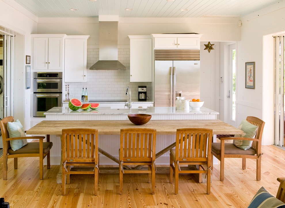 Inspiration for a large beach style galley open plan kitchen in Tampa with shaker cabinets, white cabinets, white splashback, subway tile splashback, stainless steel appliances, medium hardwood floors, with island and marble benchtops.