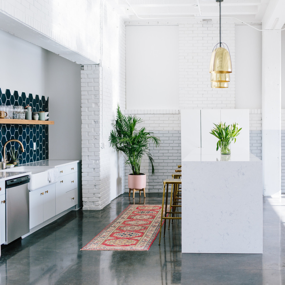 Inspiration for a mid-sized industrial kitchen in Minneapolis with a farmhouse sink, flat-panel cabinets, white cabinets, quartzite benchtops, blue splashback, ceramic splashback, concrete floors, with island and stainless steel appliances.