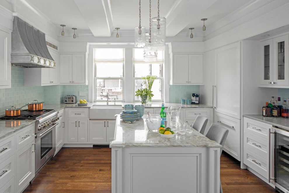 Traditional kitchen in New York with a farmhouse sink, white cabinets, marble benchtops, blue splashback, glass tile splashback, stainless steel appliances, medium hardwood floors, with island and recessed-panel cabinets.