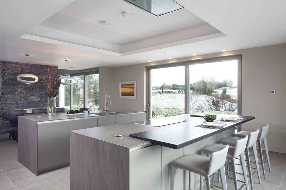 Large modern single-wall open plan kitchen in Belfast with a drop-in sink, flat-panel cabinets, beige cabinets, quartz benchtops, stainless steel appliances, ceramic floors, multiple islands and beige floor.