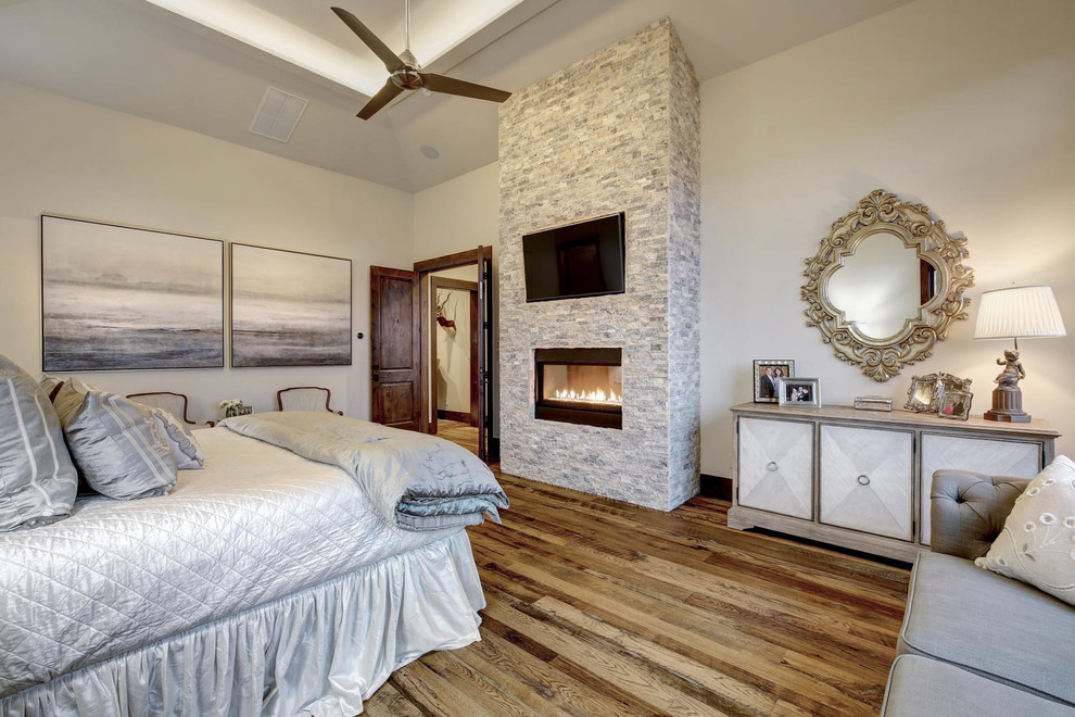 Expansive transitional master bedroom in Austin with white walls, light hardwood floors, a ribbon fireplace, a stone fireplace surround and multi-coloured floor.