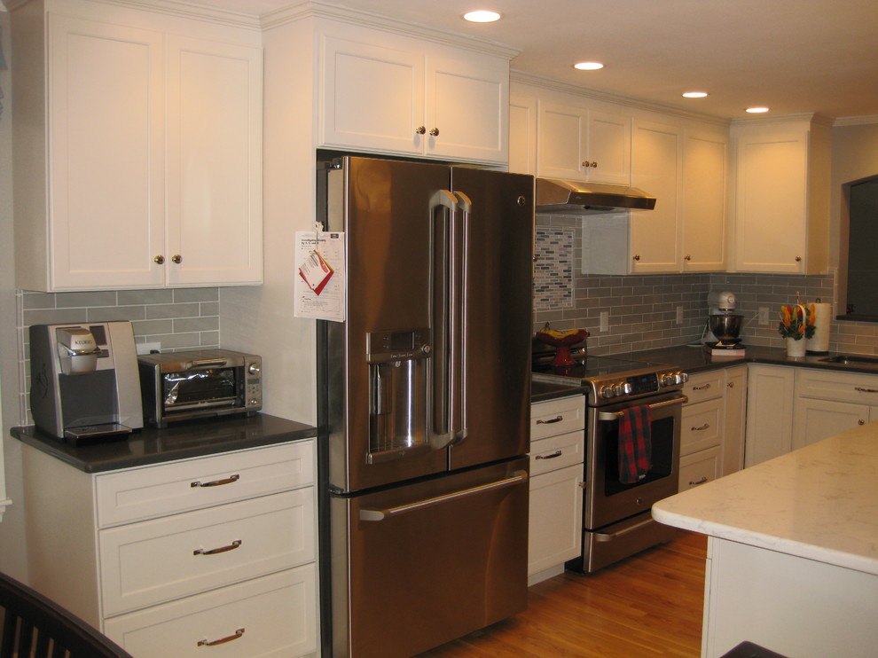 Example of a transitional l-shaped medium tone wood floor eat-in kitchen design in Boston with an undermount sink, white cabinets, quartz countertops, stainless steel appliances, an island, shaker cabinets, green backsplash, subway tile backsplash and black countertops
