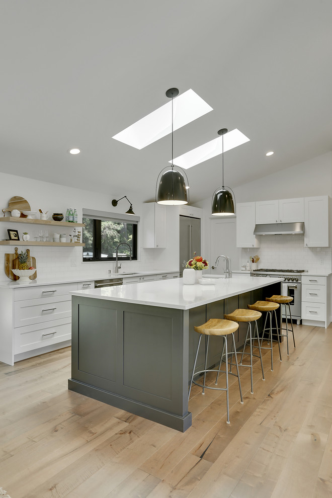 Design ideas for a transitional l-shaped kitchen in Seattle with an undermount sink, white cabinets, quartzite benchtops, white splashback, ceramic splashback, stainless steel appliances, with island, white benchtop, shaker cabinets, light hardwood floors and beige floor.