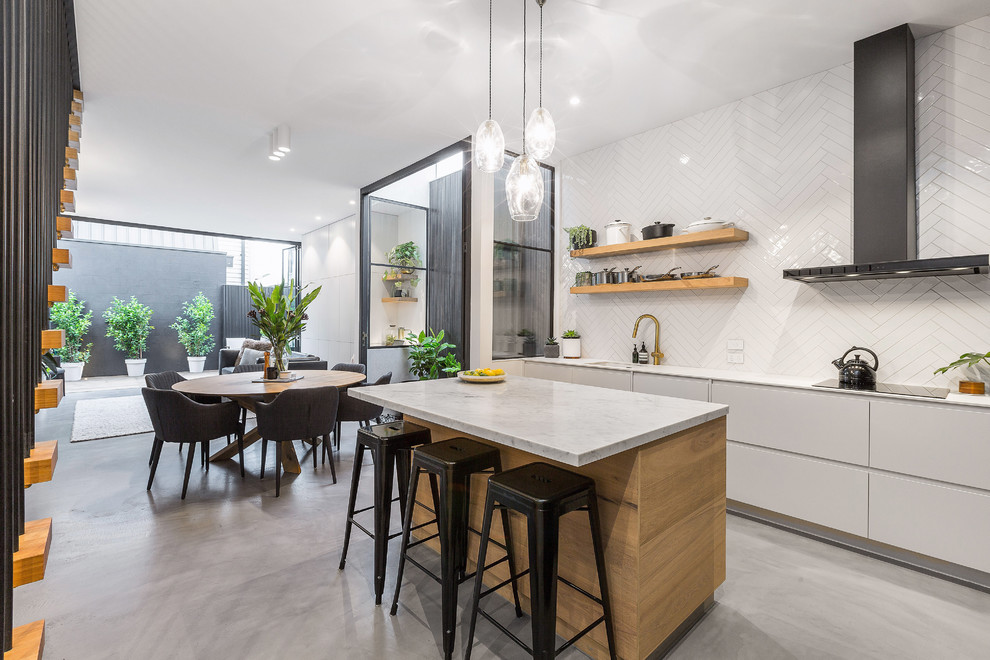 Photo of a mid-sized contemporary l-shaped eat-in kitchen in Melbourne with an undermount sink, flat-panel cabinets, white cabinets, marble benchtops, white splashback, mosaic tile splashback, black appliances, concrete floors, with island, grey floor and white benchtop.