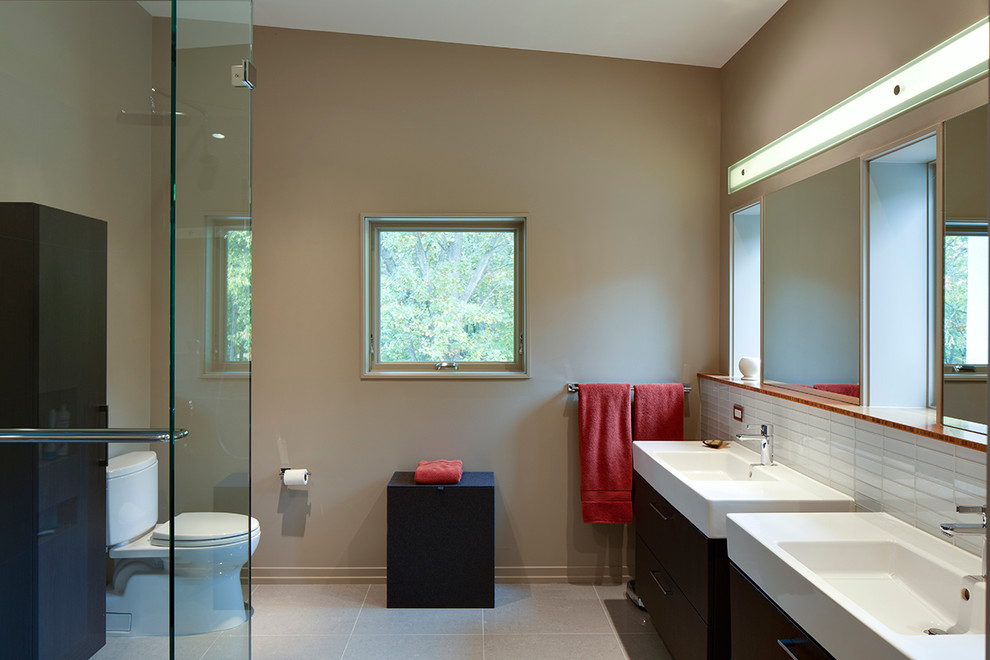 Photo of a mid-sized contemporary master bathroom in Detroit with flat-panel cabinets, dark wood cabinets, a corner shower, a two-piece toilet, white tile, glass tile, beige walls, an integrated sink, solid surface benchtops, porcelain floors, beige floor, a hinged shower door and white benchtops.