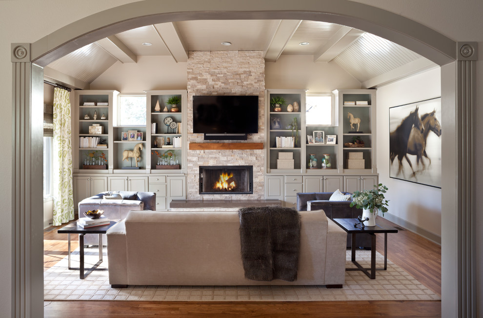 This is an example of a mid-sized transitional enclosed family room in Denver with beige walls, medium hardwood floors, a hanging fireplace, a stone fireplace surround, a wall-mounted tv and brown floor.