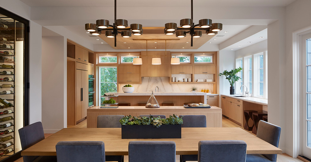 This is an example of a transitional l-shaped open plan kitchen in Minneapolis with multiple islands, flat-panel cabinets, light wood cabinets, marble benchtops, white splashback, marble splashback, stainless steel appliances and light hardwood floors.