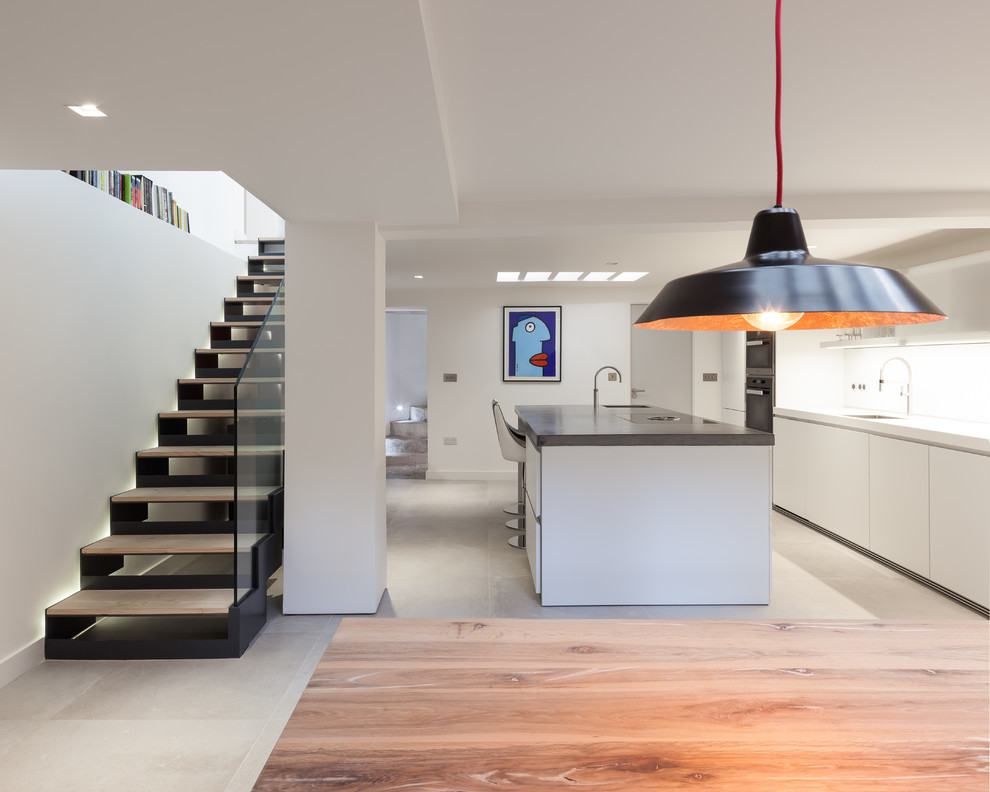 This is an example of a mid-sized contemporary single-wall open plan kitchen in London with an undermount sink, flat-panel cabinets, white cabinets, concrete benchtops, white splashback, glass sheet splashback, stainless steel appliances, cement tiles, with island, grey floor and grey benchtop.